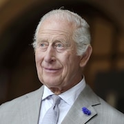Le roi Charles III a le regard tourné vers la gauche de l'image. Il porte une chemise blanche, une veste de costume et une cravate grise
