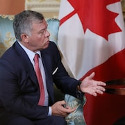 Le roi est assis dans un fauteuil devant le drapeau canadien.