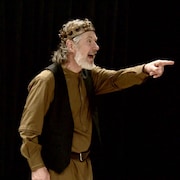 Bruce McKay dans le rôle du roi Lear, vêtu d'une couronne, pointe du doigt, son visage exprimant la surprise.