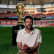 Il s'agit d'un montage de deux photos. En arri&egrave;re-plan, un stade de soccer avec le troph&eacute;e du vainqueur de la Coupe de monde de la FIFA. En avant-plan, un homme, le journaliste Romain Schu&eacute;, il regarde l'objectif de la cam&eacute;ra en mode explication.