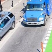 Une piste cyclable séparée d'une route où se trouvent un camion et une voiture. 