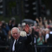 Le roi Charles III lève la main et salue la foule. 