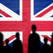 Silhouette d'immigrants illégaux devant un immense drapeau de la Grande-Bretagne peint sur un mur de briques.