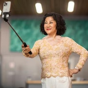 Une femme prend une photo avec un selfie stick, avec un gros sourire.