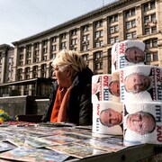 Une femme assise devant des rouleaux de papier de toilette avec le visage de Vladimir Poutine.
