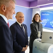 Vladimir Poutine est en compagnie de German Gref et d'une femme dans une salle où se trouvent des écrans et un ordinateur à Moscou.