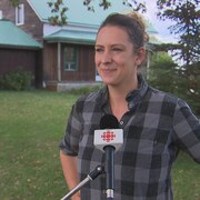 Ruth Ellen Brosseau, les mains sur les hanches, en chemise à carreaux, devant un micro de Radio-Canada.