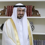 Un homme portant l'habit traditionnel saoudien et des lunettes en face d'une bibliothèque.