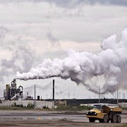 Un camion circule près d'installations qui dégagent un grand nuage de fumée.
