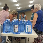 La mairesse de Saint-Pascal accueille des citoyens venus récupérer de l'eau potable. Sur la table sont préparées des dizaines de cruches d'eau. 