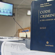 Un code criminel en avant plan, dans une salle d'audience