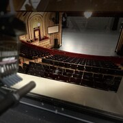 Un bout de caméra, des bancs et la scène de la salle.