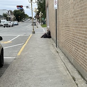 Une femme est assise sur un trottoir à Val-d'Or avec des sacs à dos.