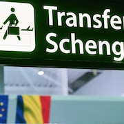 Dans un a&eacute;roport, un panneau annonce les vols en correspondance dans l'espace Schengen &agrave; c&ocirc;t&eacute; des drapeaux de l'Union europ&eacute;enne et de la Roumanie.