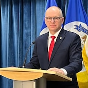 Le maire de Winnipeg Scott Gillingham en conférence de presse à l'hôtel de ville de Winnipeg, devant un rideau bleu et des drapeaux de Winnipeg, le 15 décembre 2022.