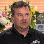 Un homme aux cheveux bruns porte un chandail noir. 