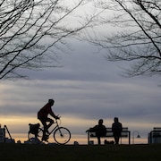 Un cycliste et des personnes assis sur un banc de parc à Vancouver au coucher du soleil. 