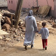 Une femme et sa fille marchent sur des des débris du séisme au Maroc.