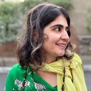 Une jeune femme aux cheveux bruns, portant un foulard jaune sur le cou, regarde à gauche.