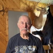 Serge Guitard dans son salon. Derrière lui, des têtes de chevreuil et une peau d'ours.