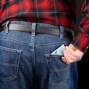 Un homme photographié de dos met un billet de 5 $ dans la poche arrière de son jean.