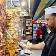Un employé d'un restaurant de shawarma coupe du poulet sur une broche. 