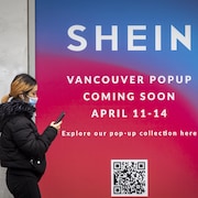 Une jeune femme marche devant un panneau publicitaire de l'entreprise Shein, qui ouvre une boutique temporaire à Vancouver.