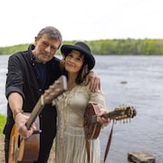 Lenny Gallant et Patricia Richard, guitare à la main, devant une rivière.