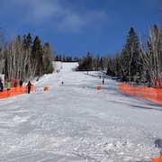 Des skieurs descendent sur une piste de ski alpin au Mont Kanasuta devant des spectateurs.