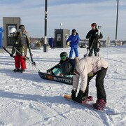 Des gens préparent leurs skis et leur planche à neige au sommet d'une piste enneigée.