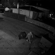 Un homme déplace un bac à ordures en plein milieu de la nuit dans une allée. 