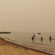 Des gens sur une plage avec un ciel gris et jaune en raison de la fumée.