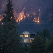 Une maison dont les lumières intérieures sont allumées, avec un feu de forêt à l'arrière, le 18 août 2023. 