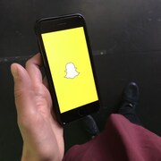 Un téléphone mobile dans une main avec le logo de Snapchat sur le téléphone. 