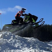 Un motoneigiste effectue un saut sur une butte de neige aux commandes de son engin.