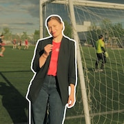 La journaliste Victoria Kopiloff un micro &agrave; la main, appuyer contre des cages d'un terrain de soccer.