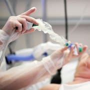 Une personne est couchée dans un lit d'hôpital et on voit les mains d'une infirmière qui prépare un tube.
