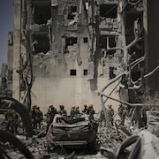 Des soldats à l'œuvre devant un édifice endommagé par un missile.
