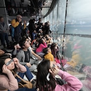 Des dizaines de personnes face aux vitres de la tour CN et avec des lunettes de protection.