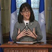 Sonia LeBel donne un point de presse à l’Assemblée nationale. Elle se tient debout, derrière un lutrin et devant des drapeaux du Québec.