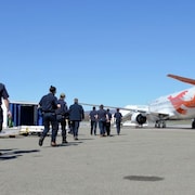 Des pompiers en uniforme se dirigent vers un avion pour l'embarquer. 