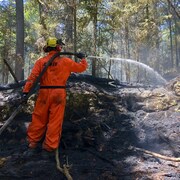 Un pompier de la SOPFEU qui arrose le sol dans une forêt.