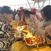 Des femmes déposent de la nourriture dans les assiettes des personnes qui font la file au souper communautaire.