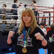 Emily Vigneault, les poings levés, avec une médaille d'or au cou, dans un gymnase.