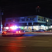 Deux camionnettes de la police sont garées devant un immeuble commercial durant la nuit. La rue est délimitée par un périmètre de sécurité.