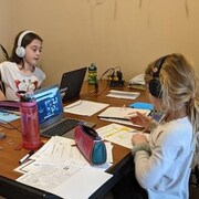 Deux fillettes à une table suivent chacune leur professeur sur leur ordinateur.