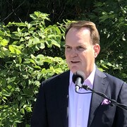 Le député MacKinnon pendant une conférence de presse devant des arbres. 