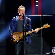 Sting joue de la guitare basse sur scène.