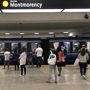 Une rame de métro passe tandis que des usagers attendent sur le quai.
