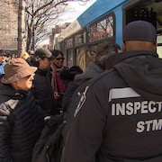 Des passagers en file pour monter dans un bus, sous les yeux d'un inspecteur de la STM.